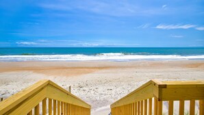A wooden staircase leading to a beach with a clear blue sky and ocean view. - Beachfront home with private heated pool, hot tub, & elevator (North Topsail Beach)