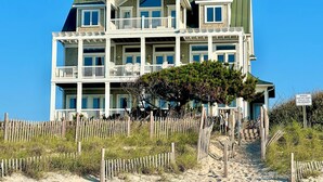 A multi-story beachfront hotel with balconies, a wooden fence, and a warning sign. - Beachfront home with private heated pool, hot tub, & elevator (North Topsail Beach)