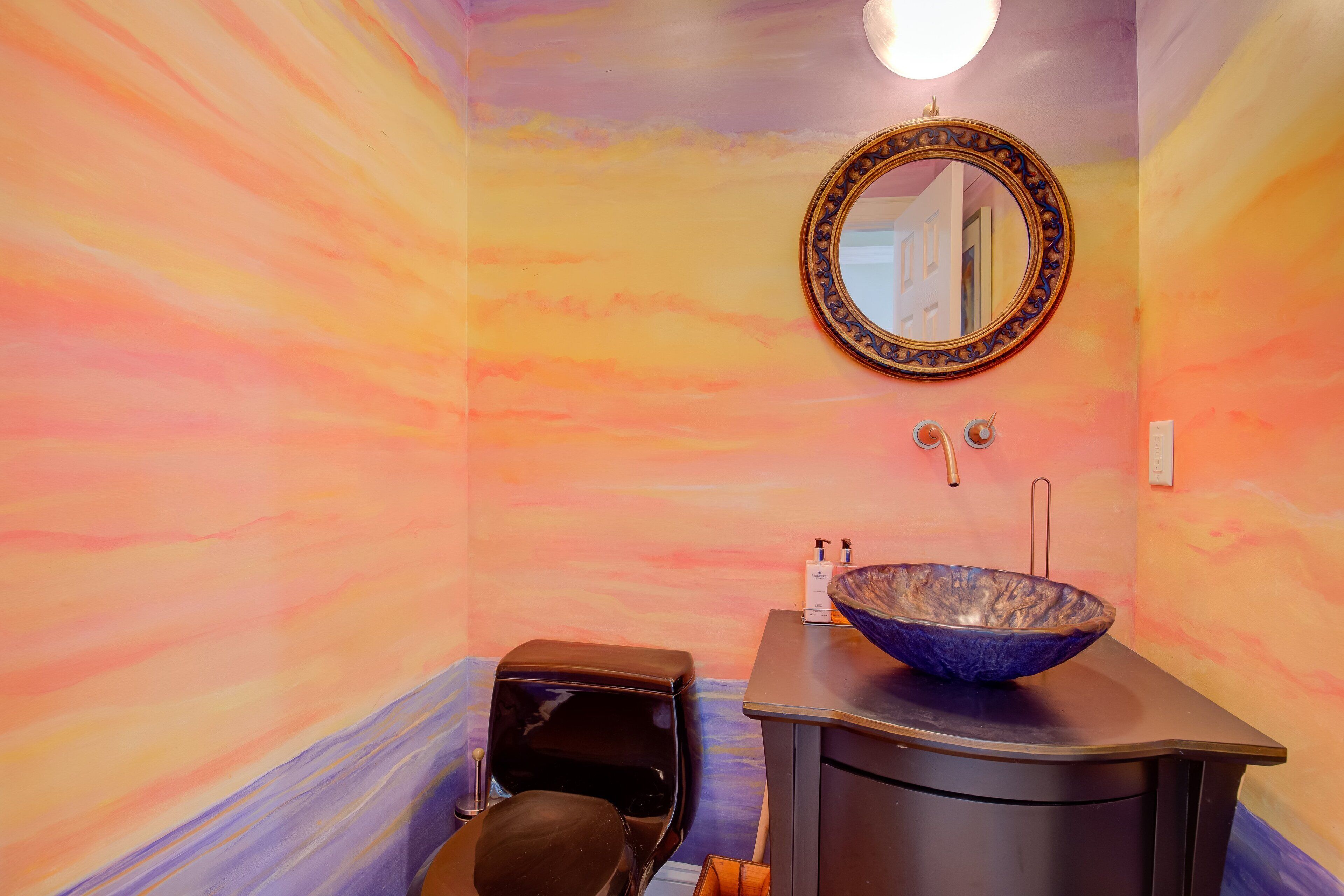 Un bagno con un grande specchio rotondo, un water nero e un mobile lavabo con lavandino blu.