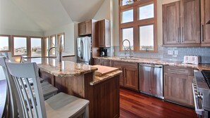 Una cocina moderna con armarios de madera, encimera de granito, electrodomésticos de acero inoxidable y grandes ventanas con vistas a la ciudad.