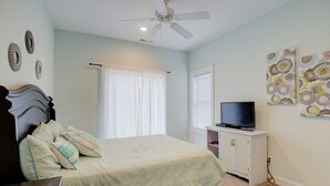 Un dormitorio con cama, televisor sobre un mueble, ventilador de techo y decoración en las paredes.