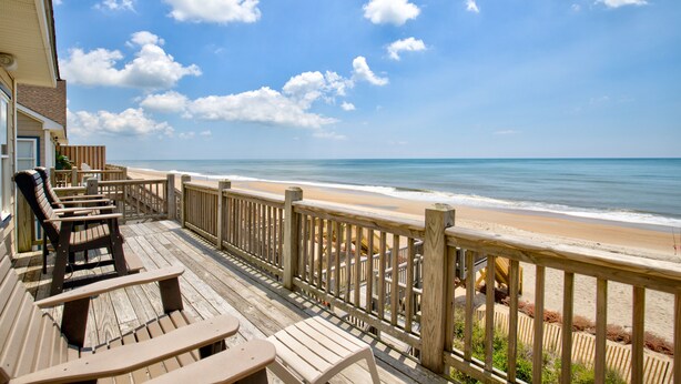 Una terraza de madera con sillas y mesas con vista a la playa.