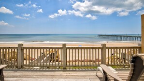 Una terraza de madera con vista a la playa y al muelle.