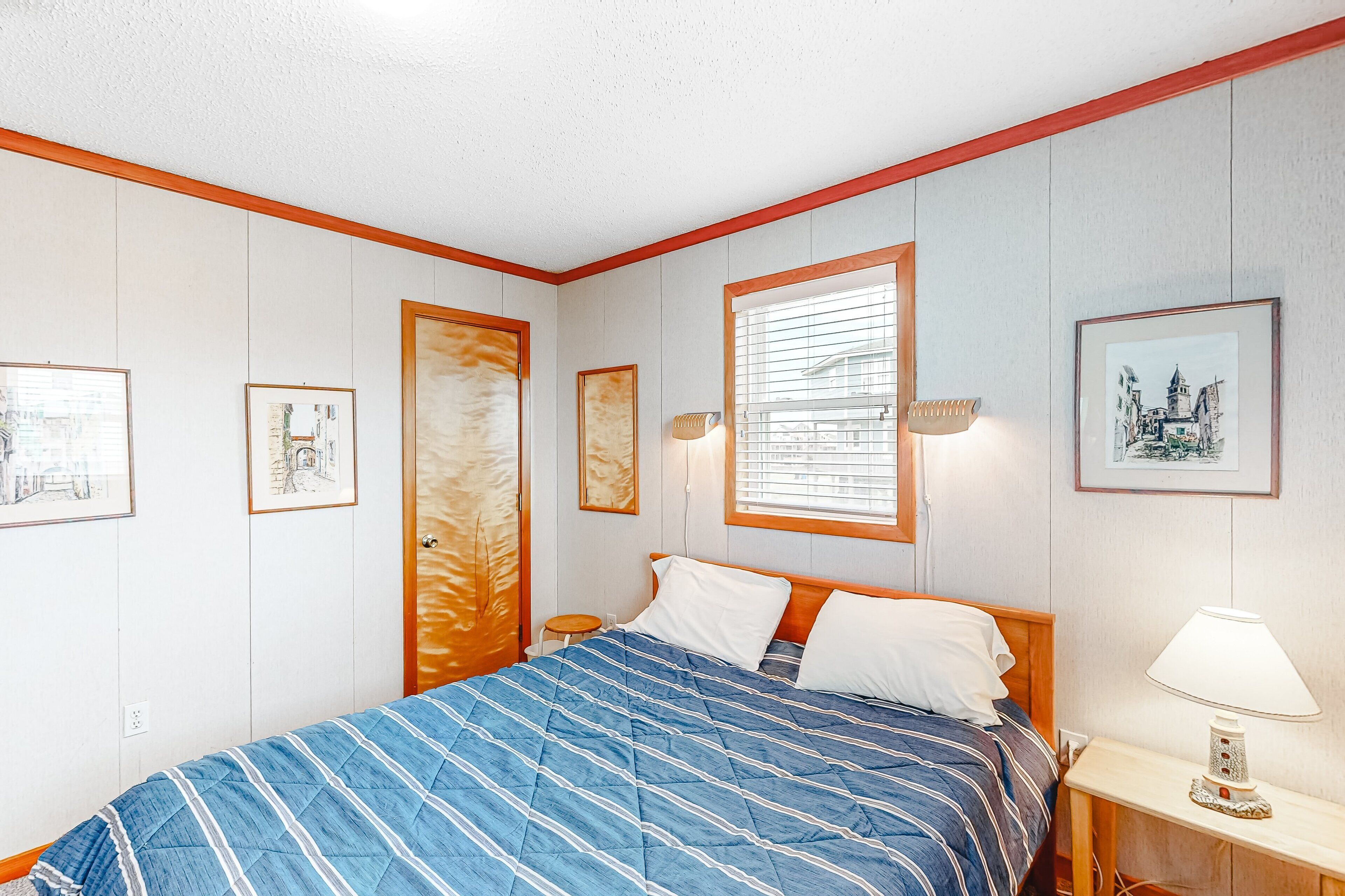 A bedroom with a bed, a nightstand, a lamp, and framed pictures on the walls.