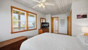A bedroom with a large bed, a ceiling fan, a wooden dresser, a television, and a door leading to another room. - Light-filled canal front home w/deck, washer/dryer, private hot tub, central A/C (Frisco)