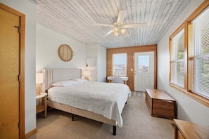 A bedroom with a bed, bedside tables, a desk, a chair, a ceiling fan, and a window with blinds.