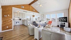 A spacious living area with a kitchen, a grey sofa, and a television. - Light-filled canal front home w/deck, washer/dryer, private hot tub, central A/C (Frisco)