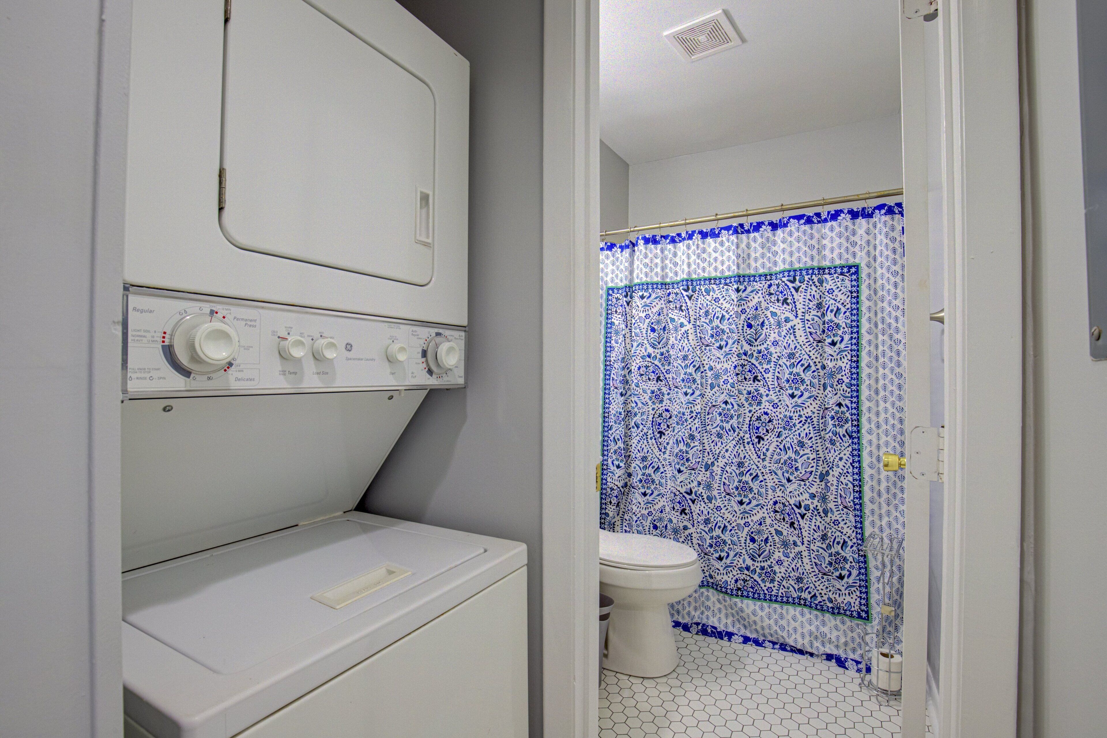 Een kleine badkamer met een wasmachine, toilet en douchegedeelte met een decoratief tegelpatroon.