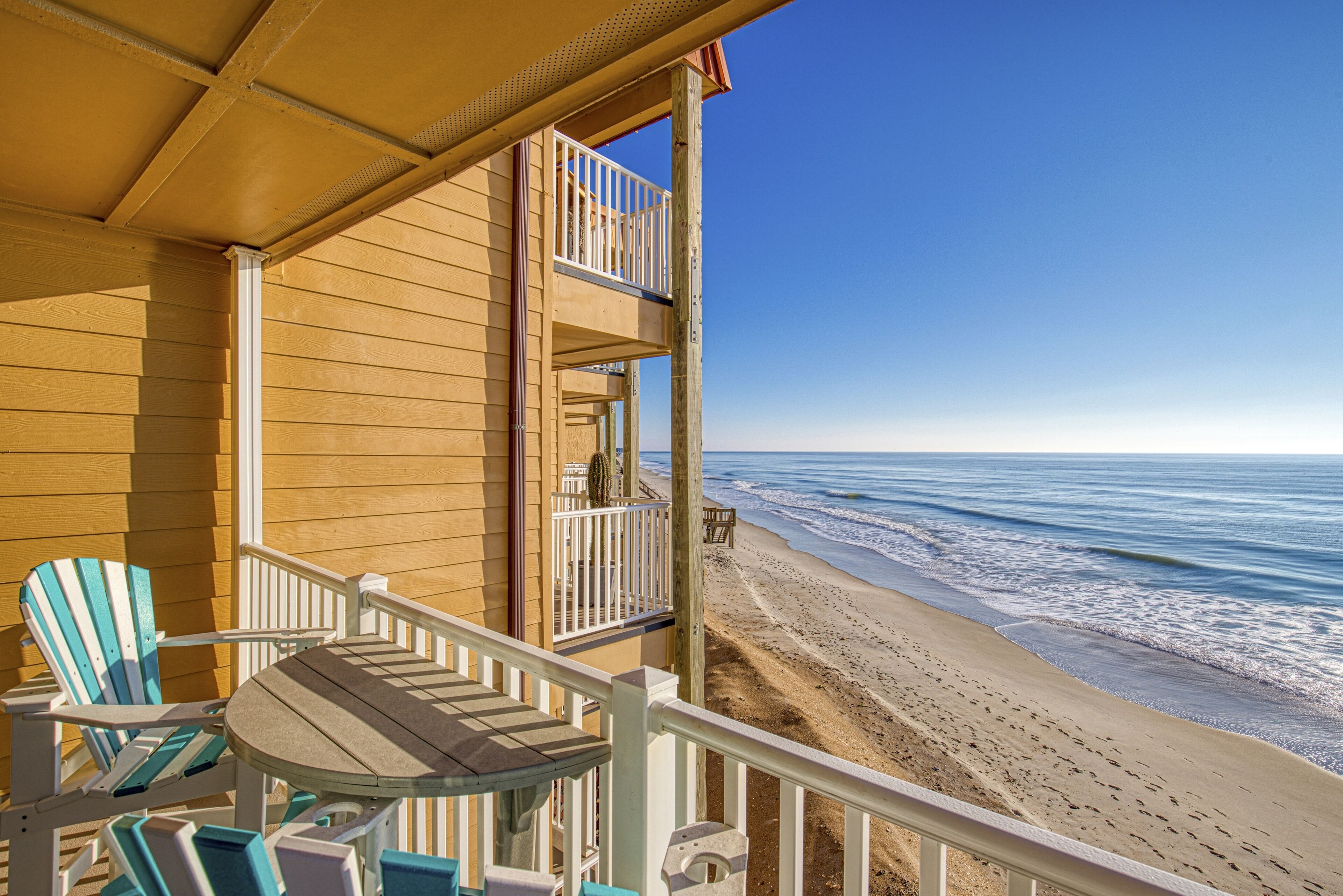 Ein Ferienhaus direkt am Strand mit einem Balkon und Meerblick, ausgestattet mit Holzmöbeln und freiem Blick auf den Strand.