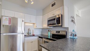 A modern kitchen with white cabinets, stainless steel appliances, and a granite countertop. - Topsail Dunes condo - ocean-view balcony - beach access & beachfront pool (North Topsail Beach)