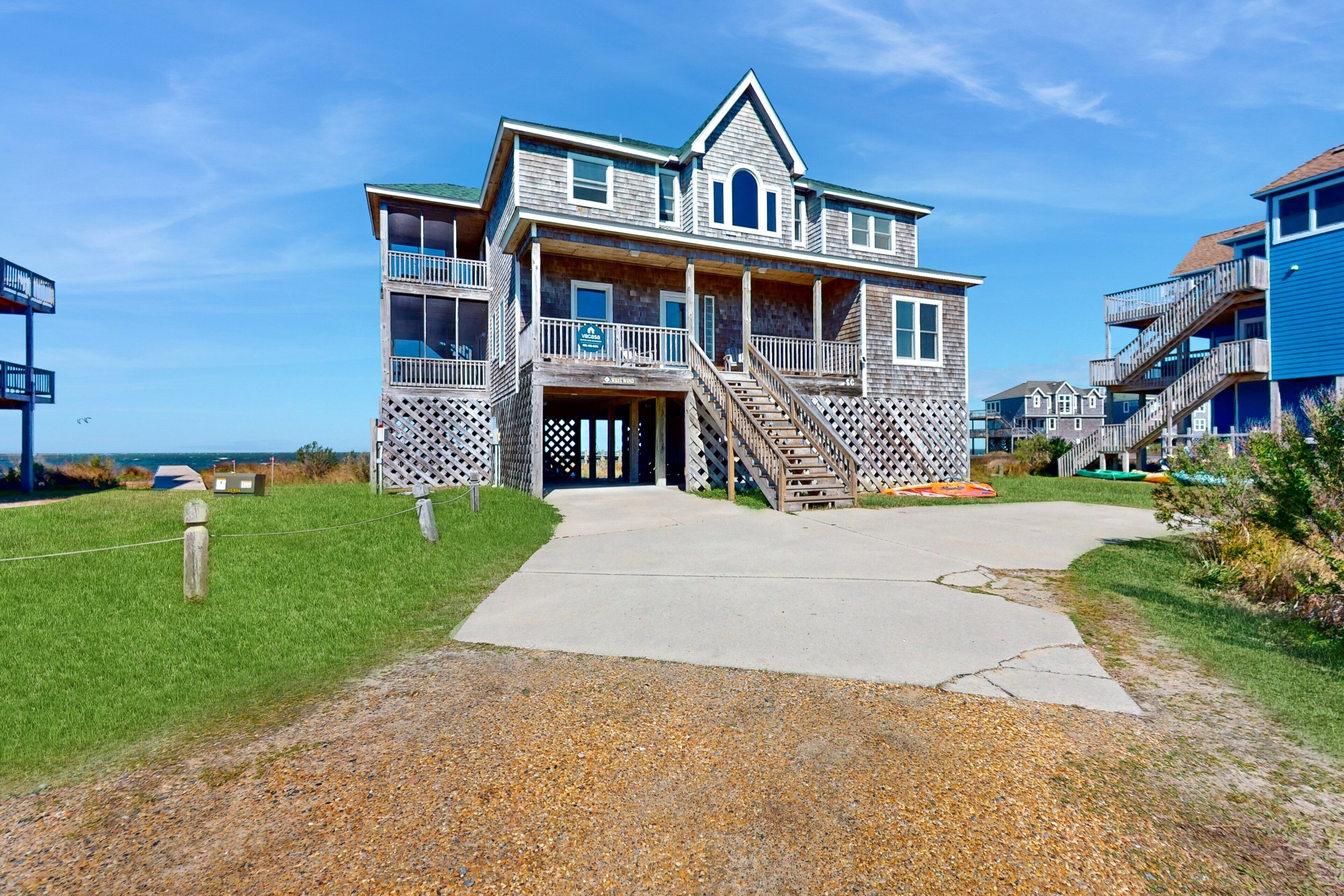 A two-story wooden building with a balcony, a staircase leading to the entrance, and a clear view of the ocean.