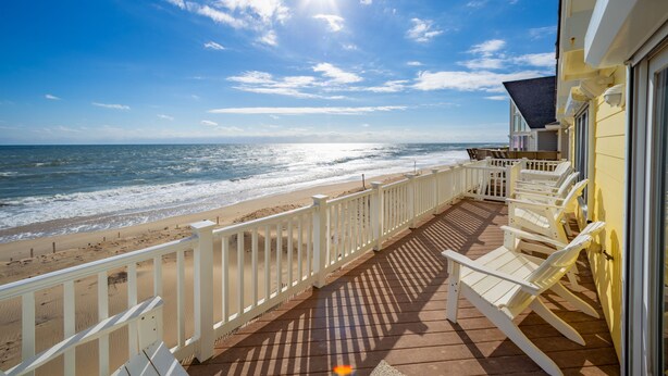 Blick auf einen Strand von einem Balkon mit weißen Geländern und Liegestühlen.