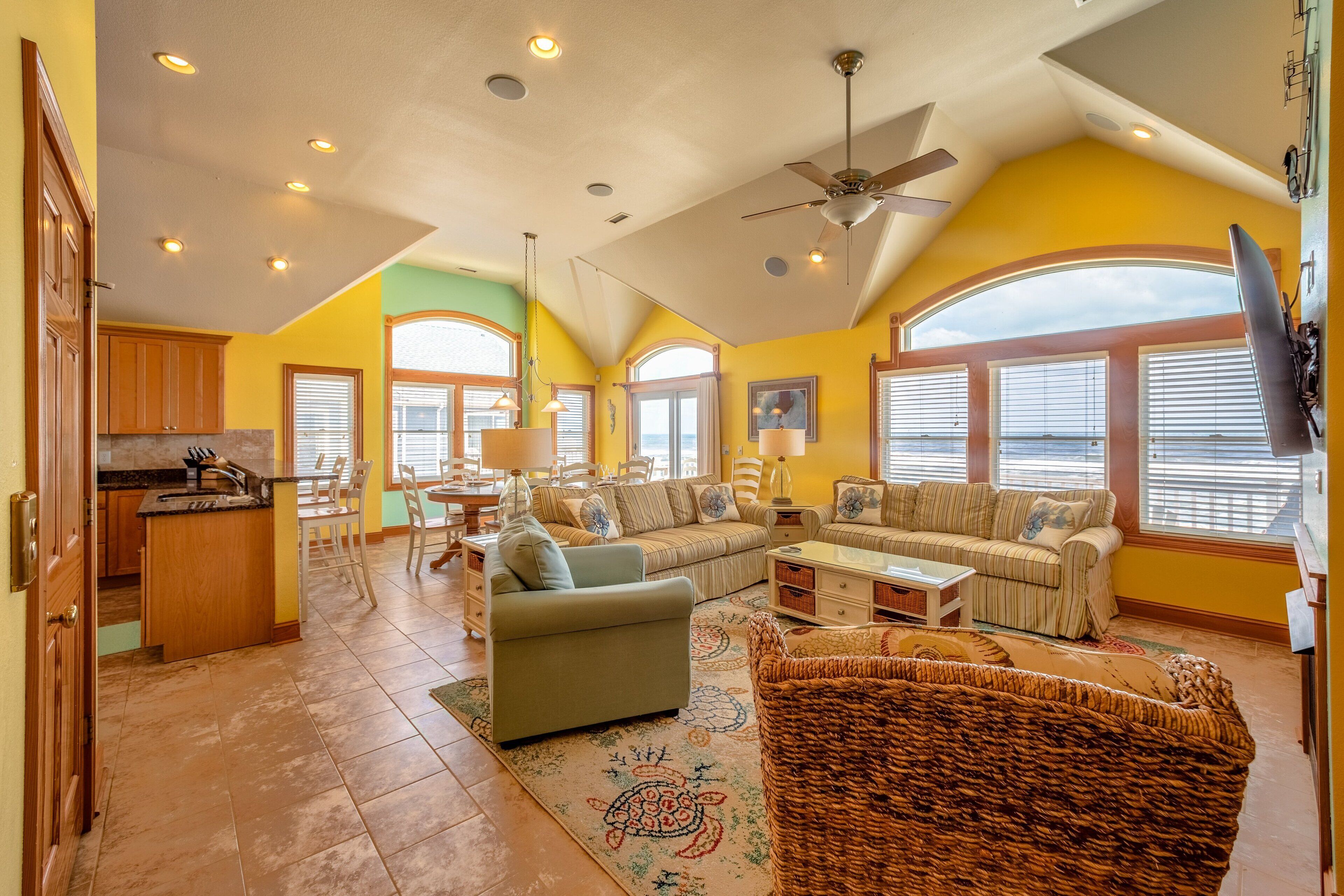 A spacious living area with a large sofa, a dining table, and a kitchen area with wooden cabinets and a tiled floor.