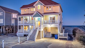 Ein zweistöckiges Strandhaus mit Balkon, einer Treppe zum Eingang und Blick auf den Strand.