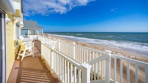 Ein Strandhaus mit Holzterrasse und weißen Geländern mit Blick auf den Ozean.