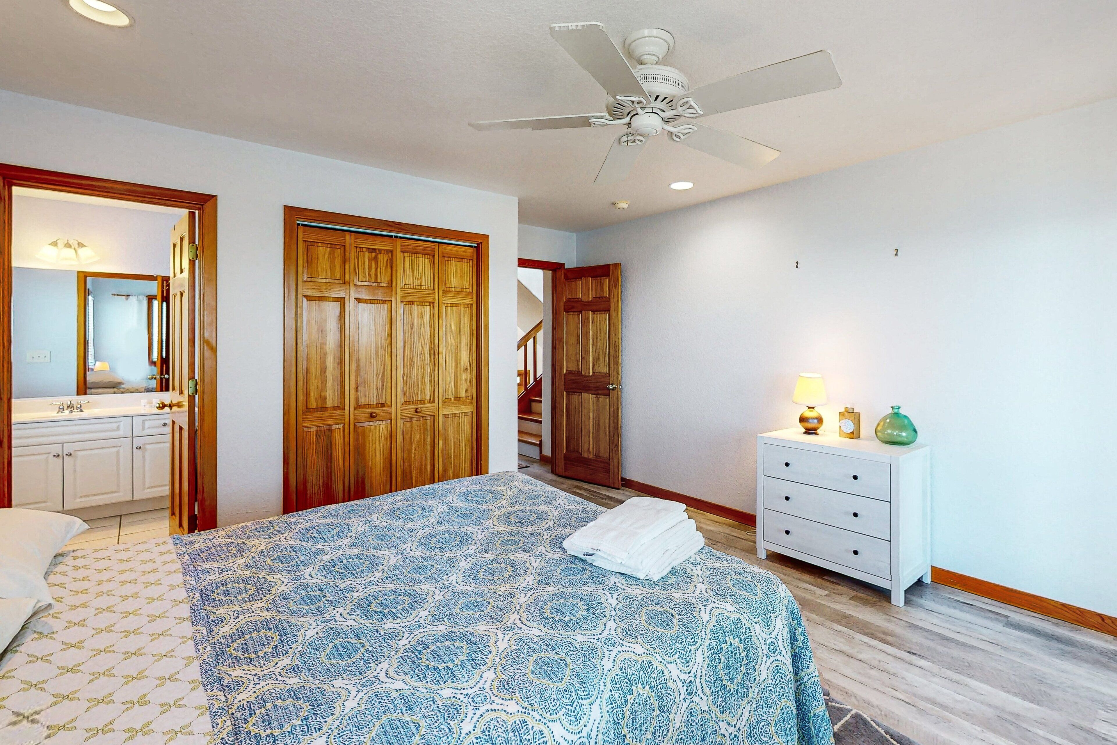 A bedroom with a bed, wooden wardrobe, white dresser, and a ceiling fan.