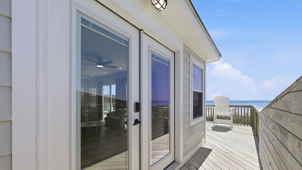 Une terrasse en bois avec une porte vitrée donnant sur une pièce, un ventilateur de plafond et une vue sur l’océan.