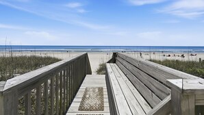 Une promenade en bois menant à une plage, avec un ciel dégagé.