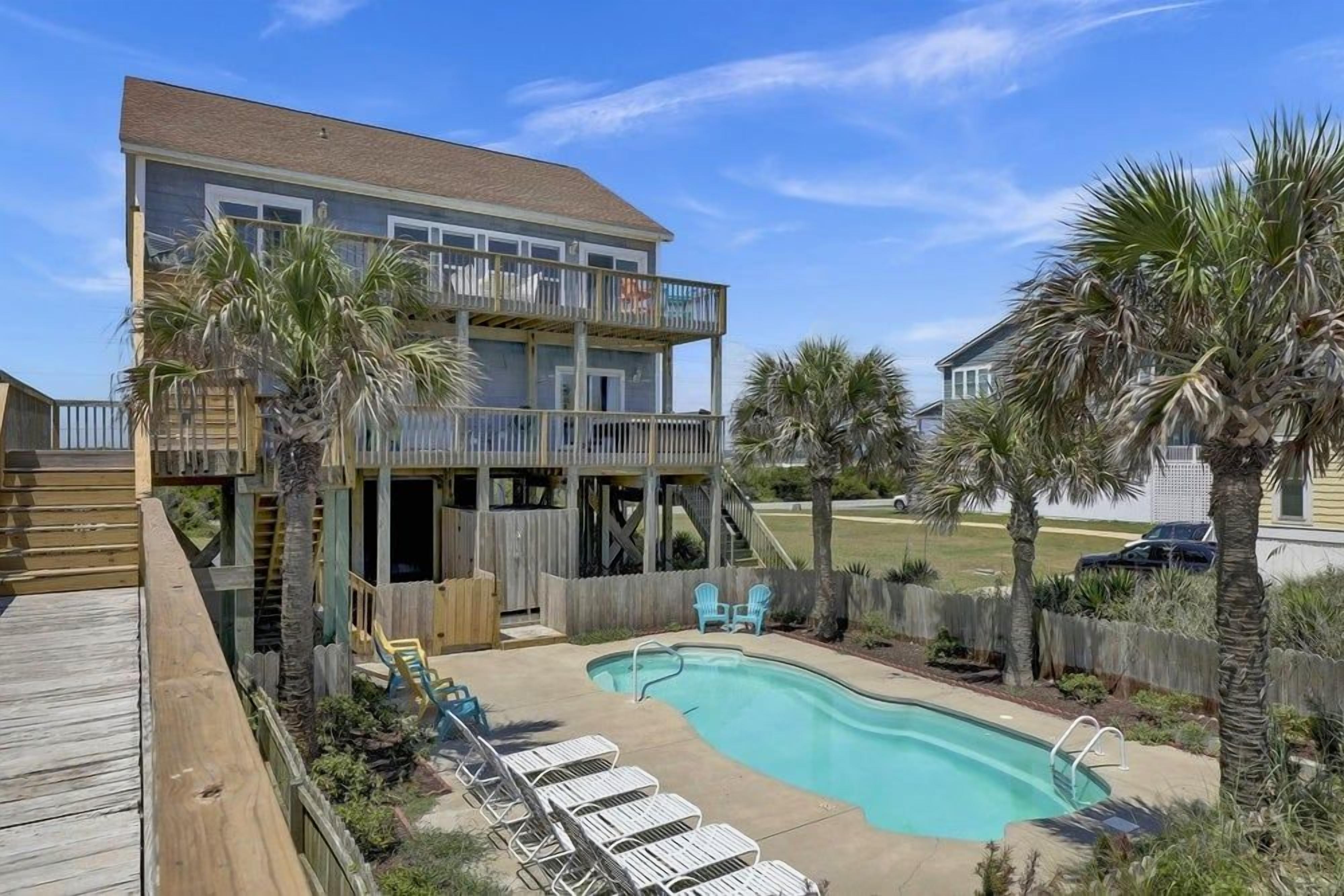 Une maison à deux étages avec une piscine, une terrasse en bois et un espace salon extérieur.
