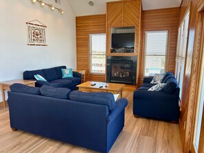 A living room with a fireplace, two sofas, a coffee table, and a TV. - Ocean-view home with central AC, pool, & hot tub (Buxton)
