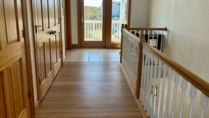 A hallway with wooden doors, a white railing, and a view of the outside. - Ocean-view home with central AC, pool, & hot tub (Buxton)