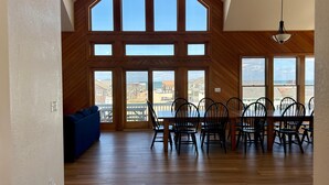 A spacious room with a high ceiling, large windows, a dining area with chairs, and a blue sofa. - Ocean-view home with central AC, pool, & hot tub (Buxton)