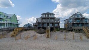 A beachfront property with multiple levels, wooden walkways, and a sandy beach. - Beachfront, multi-level home with pool, beach access & private hot tub (North Topsail Beach)