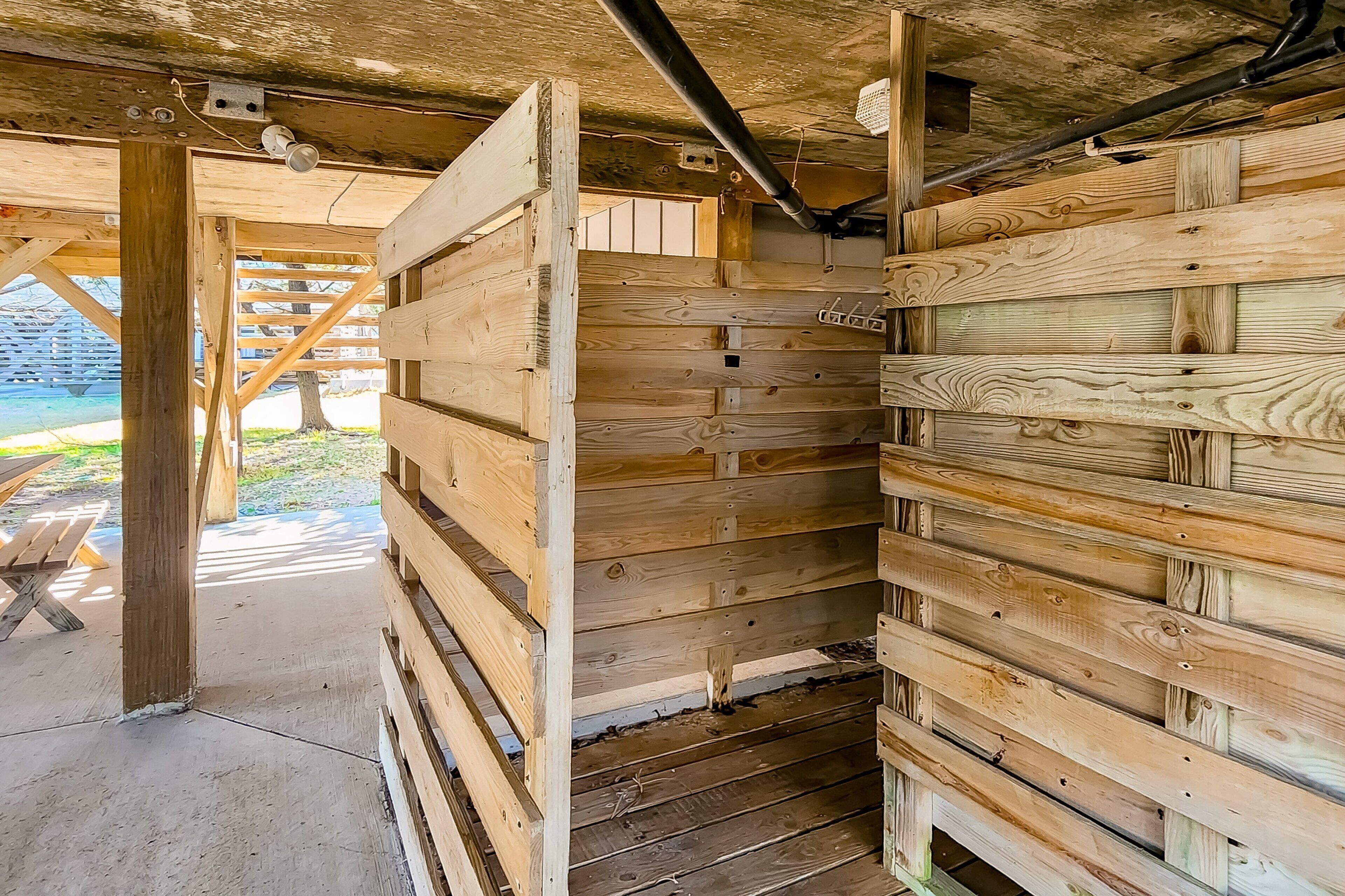 A wooden cabin with a sloped roof, visible beams, and a concrete floor.