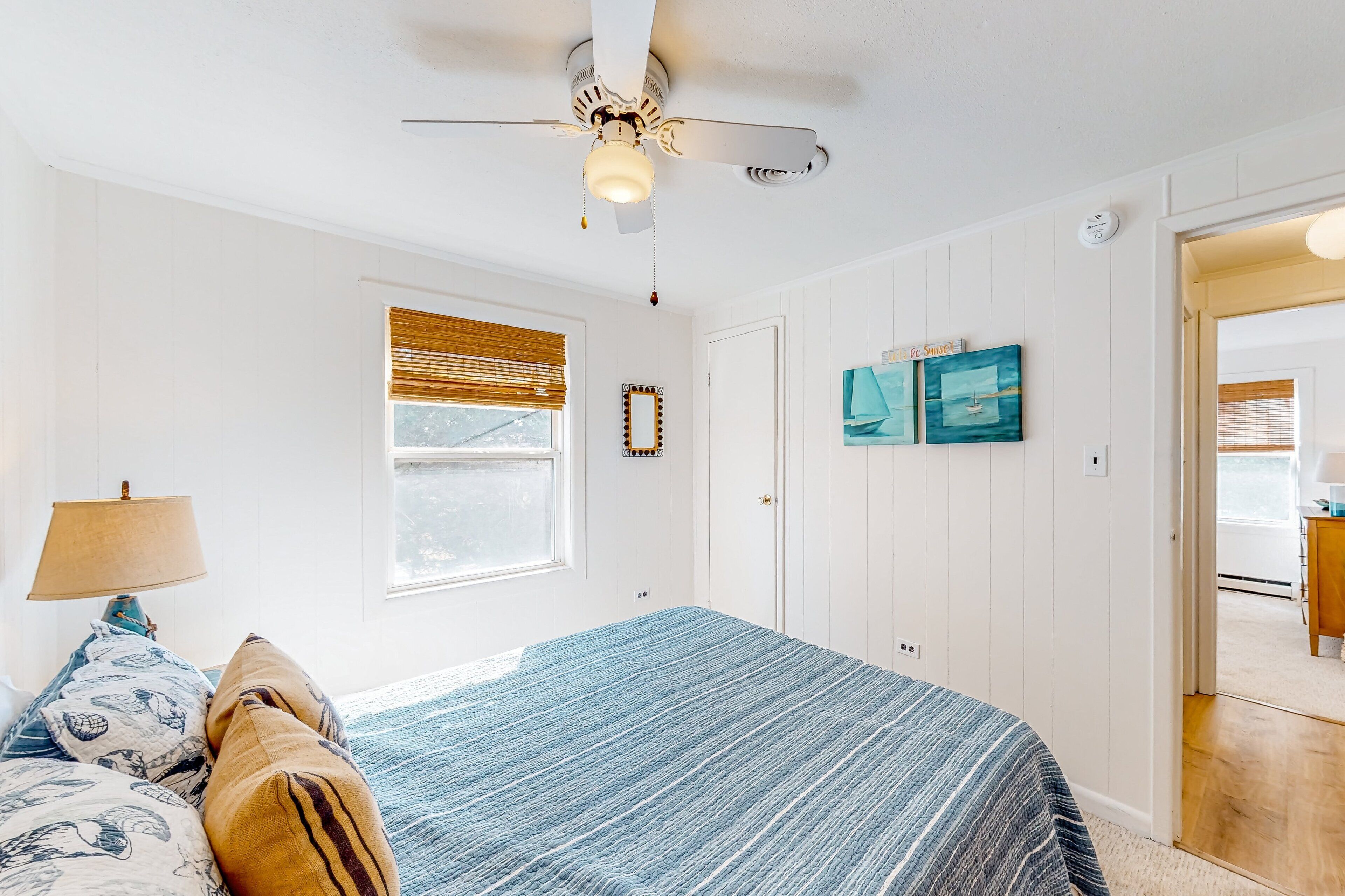 A bedroom with a bed, a ceiling fan, a window with blinds, and a door leading to another room.