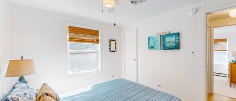 A bedroom with a bed, a ceiling fan, a window with blinds, and a door leading to another room.