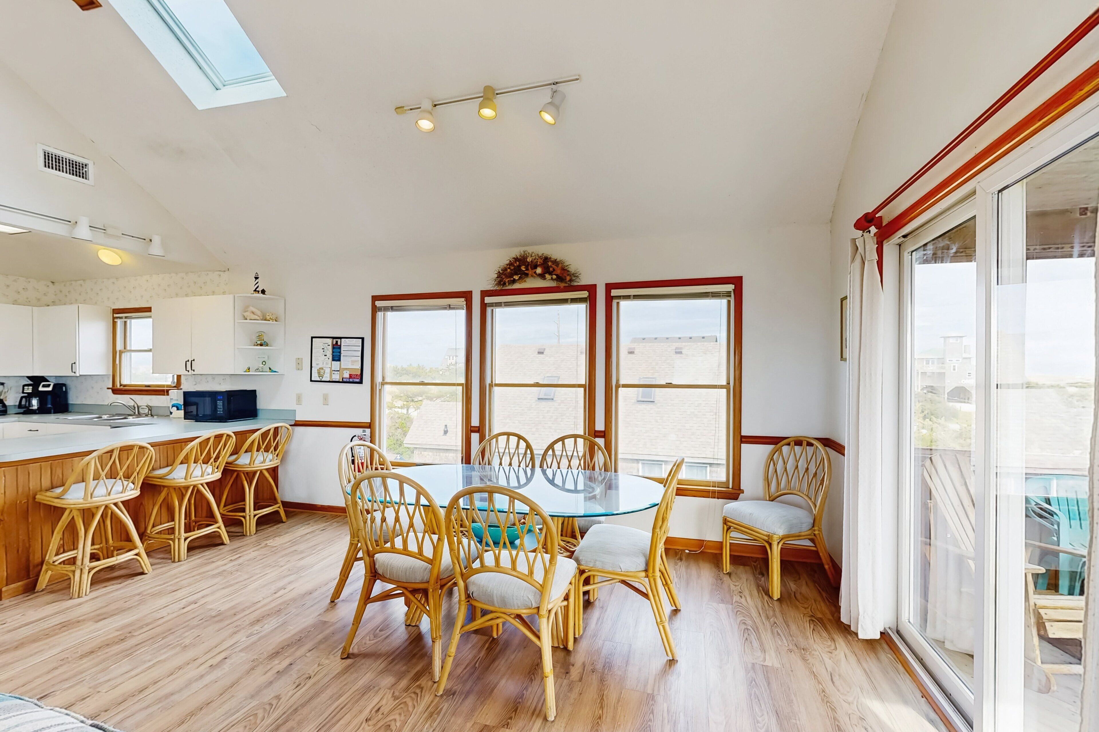 A spacious kitchen with a central island, wooden chairs, and large windows offering views of the city.