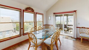 A dining area with a glass table surrounded by wicker chairs, large windows, and a view of the outside. - Blue Seas #124-A: Soundside,Private Hot Tub, Roof Deck, Water/Lighthouse Views (Avon)