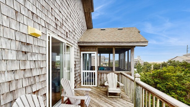 A wooden deck with Adirondack chairs, a glass door, and a view of the surrounding area. - Blue Seas #124-A: Soundside,Private Hot Tub, Roof Deck, Water/Lighthouse Views (Avon)