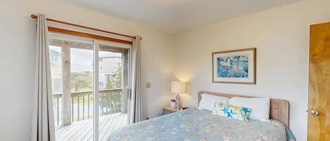 A bedroom with a bed, a nightstand, a lamp, a painting, and a sliding glass door to a balcony.