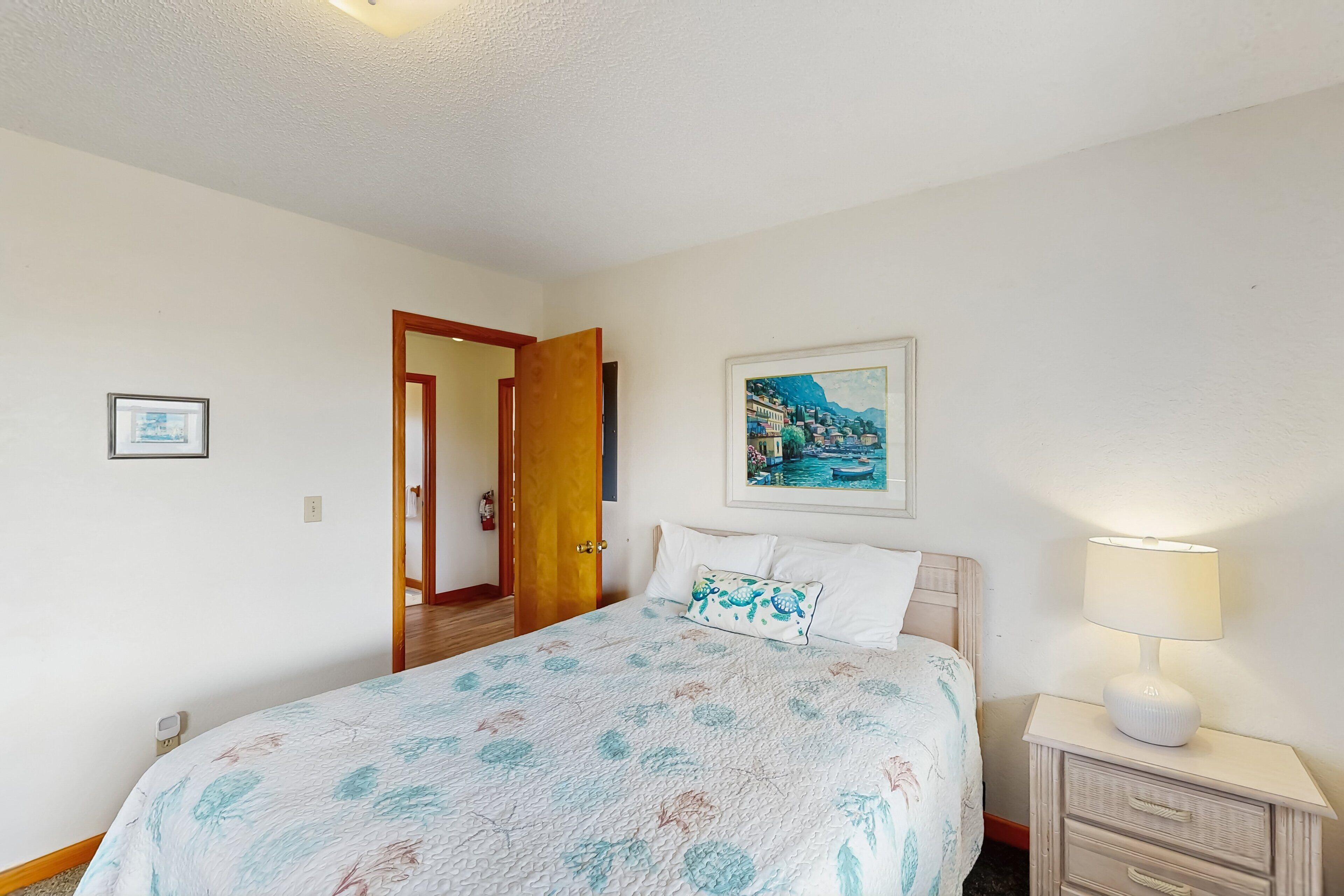 A bedroom with a bed, a nightstand, a lamp, a painting, and a door leading to another room.