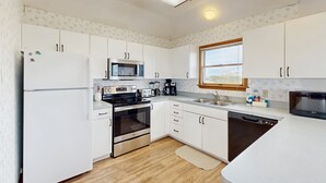 A modern kitchen with white cabinets, stainless steel appliances, and a wooden floor. - Blue Seas #124-A: Soundside,Private Hot Tub, Roof Deck, Water/Lighthouse Views (Avon)
