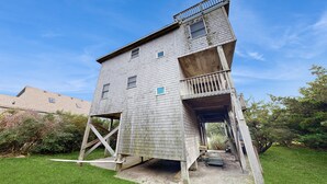 A tall, wooden tower-like structure with a balcony, surrounded by a grassy area and trees. - Blue Seas #124-A: Soundside,Private Hot Tub, Roof Deck, Water/Lighthouse Views (Avon)