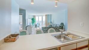Een moderne keuken met een wit aanrecht, een roestvrijstalen spoelbak en een eethoek met een tafel en stoelen.