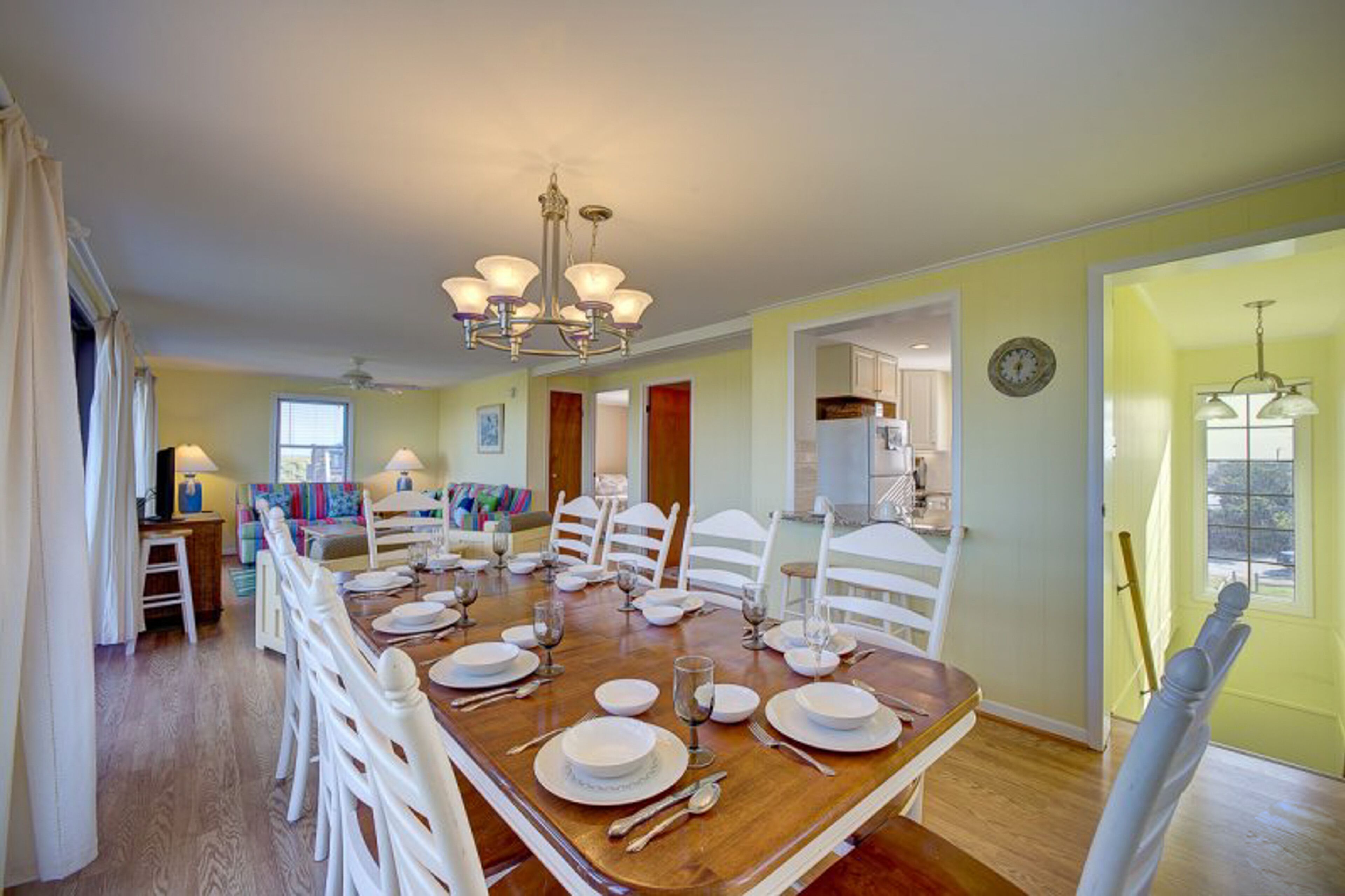 A dining room with a wooden table set for six, white chairs, and a chandelier.