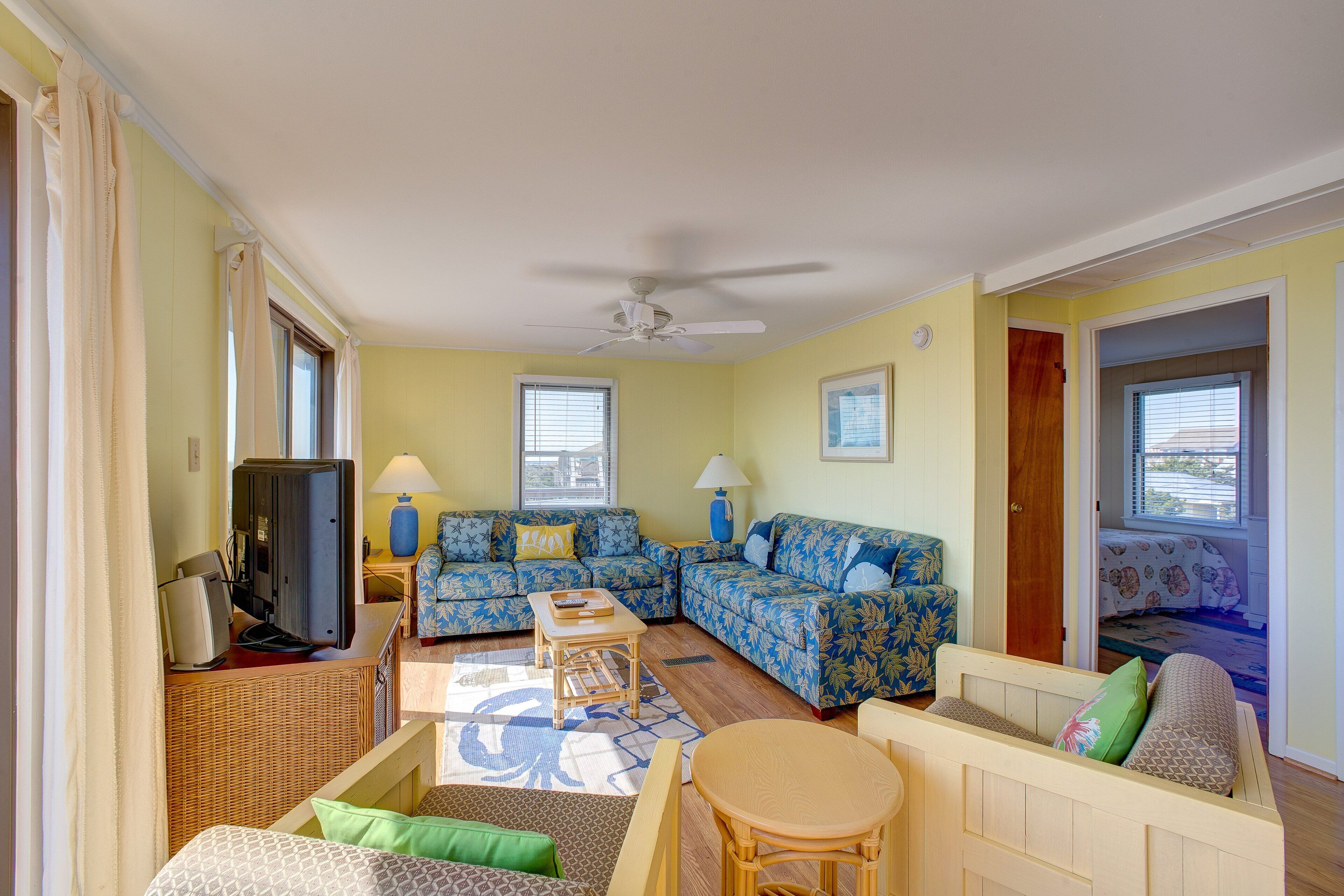 A living room with a sofa set, a television, a table, and a ceiling fan.