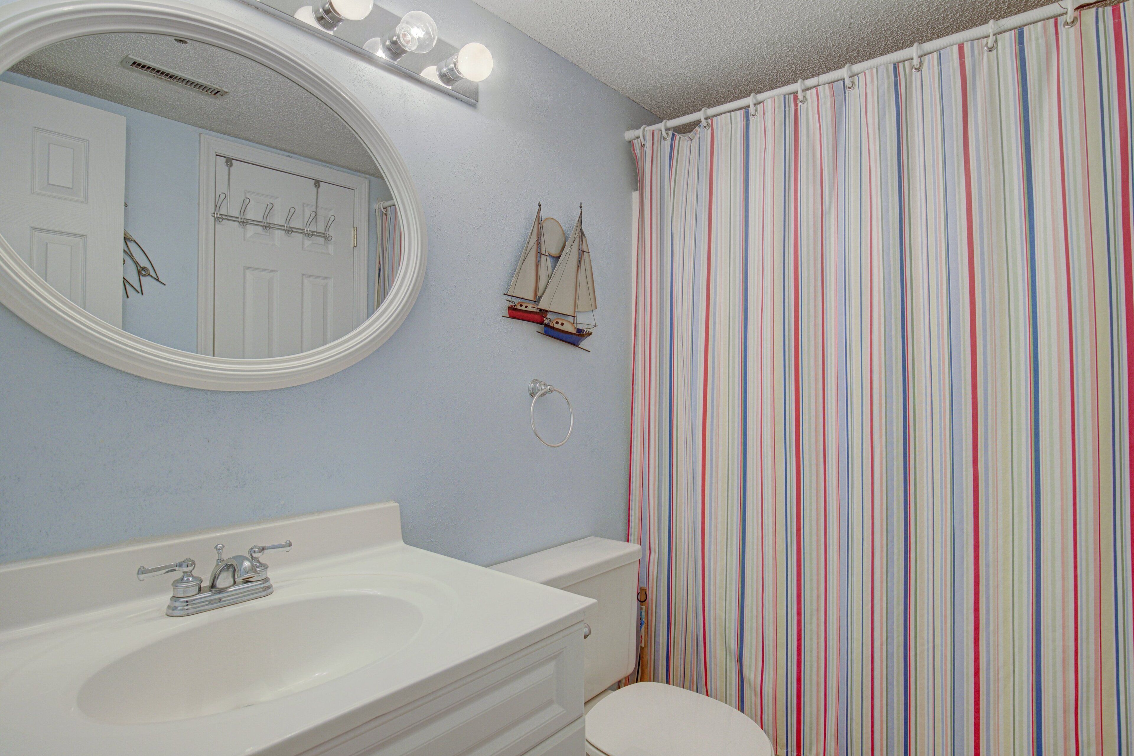A bathroom with a white sink, a mirror, a toilet, and a striped shower curtain.