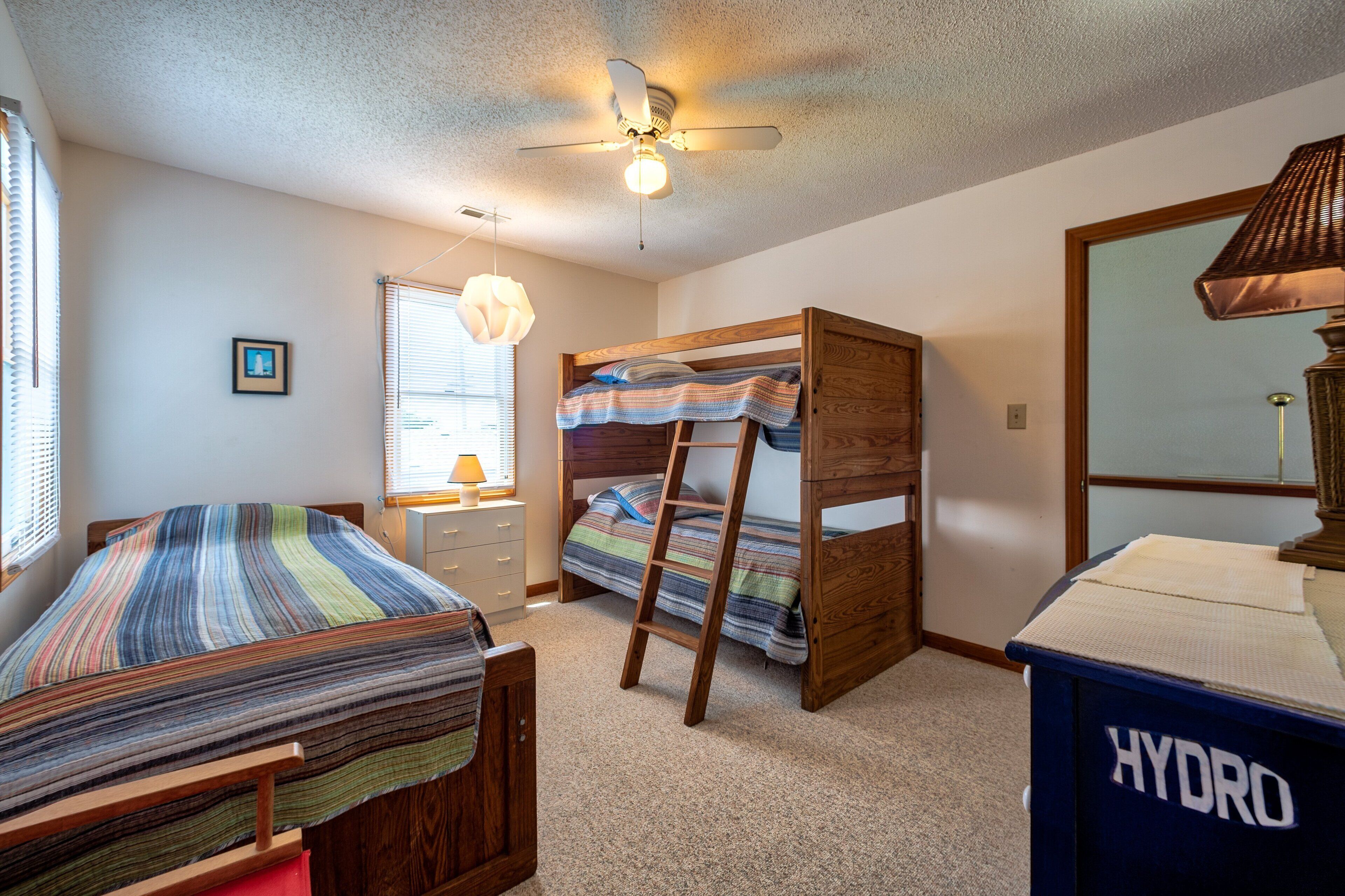 A bedroom with bunk beds, a ceiling fan, a lamp, and a blue trash bin labeled HYDRO.