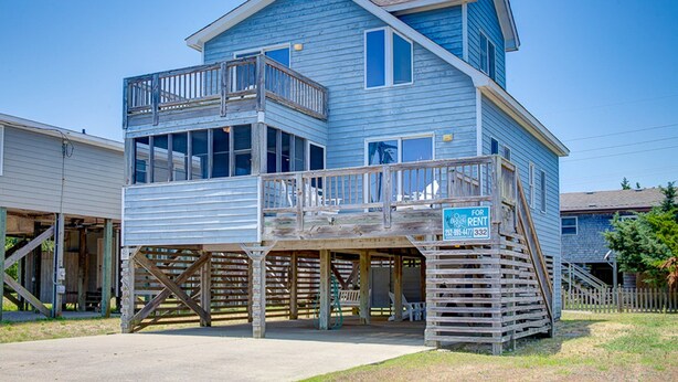 A two-story house with a balcony, a wooden deck, and a sign indicating it is for rent. - Cape Joy 332: Lovely home 5 lots from beach w/screened porch (Avon)