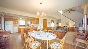 A spacious kitchen with wooden cabinets, a dining area with a round table and chairs, and a living room with a sofa and chairs. - Cape Joy 332: Lovely home 5 lots from beach w/screened porch (Avon)