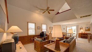 A spacious living room with wooden furniture, a ceiling fan, and a dining area with a wooden table and chairs. - Cape Joy 332: Lovely home 5 lots from beach w/screened porch (Avon)