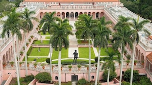 Un edifici gran amb un pati central, palmeres i una estàtua.