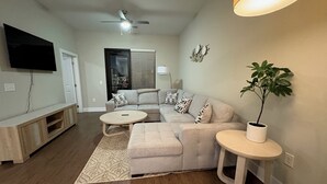 A living room with a sectional sofa, a round coffee table, a TV mounted on the wall, a ceiling fan, and a potted plant. - The Nash Luxe- In the heart of Nashville (Nashville)