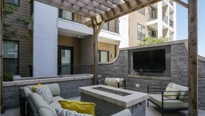 An outdoor patio with a sofa, chairs, a fire pit, and a TV mounted on a stone wall. - The Nash Luxe- In the heart of Nashville (Nashville)