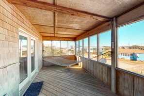 Une véranda en bois avec un hamac, de grandes fenêtres et une vue sur les environs.