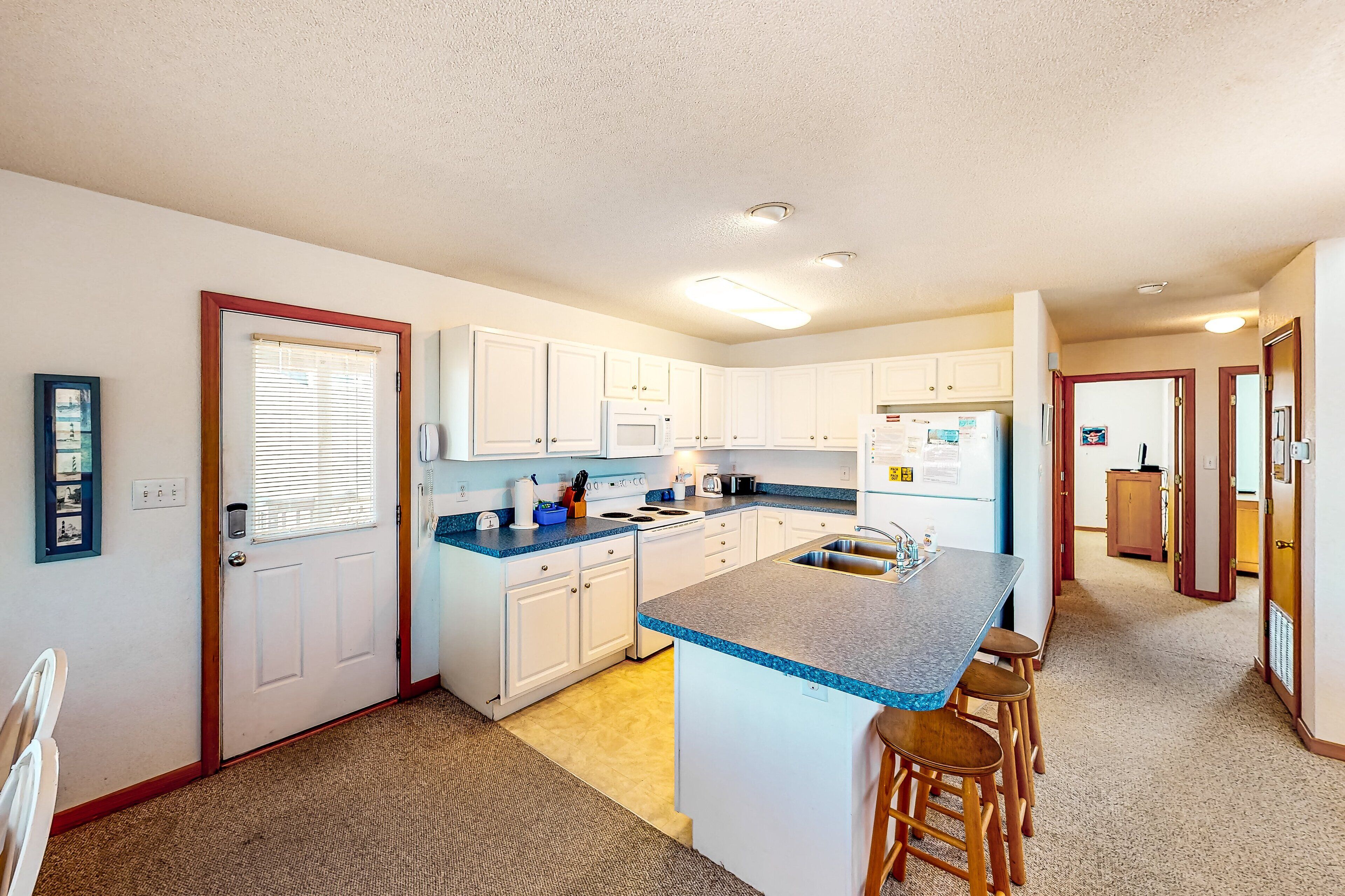 A modern kitchen with white cabinets, a blue countertop, and a central island with stools.